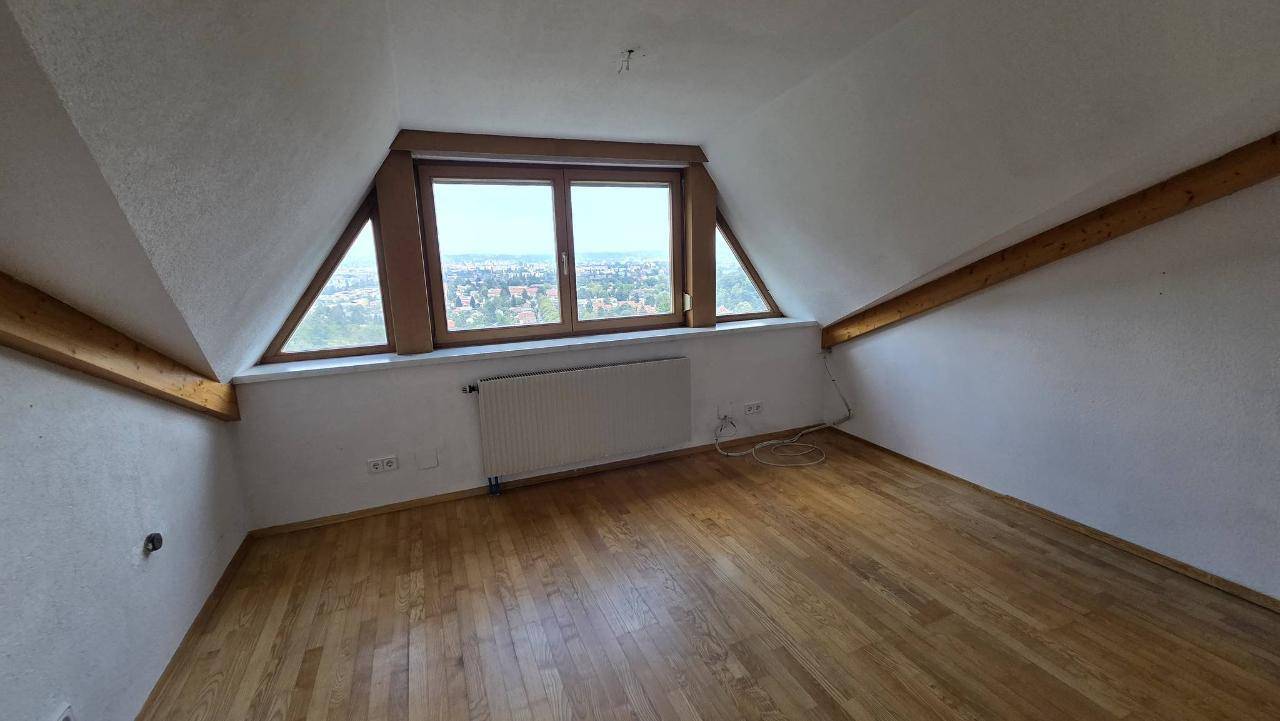 Dachgeschosszimmer mit Holzboden, schrägen Wänden und Fenstern, die einen weiten Blick bieten.