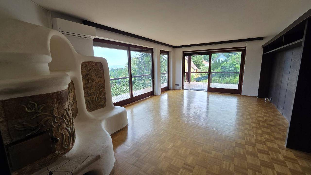 Helles Wohnzimmer mit Parkettboden, Kachelofen und großen Fenstern mit weitem Blick.