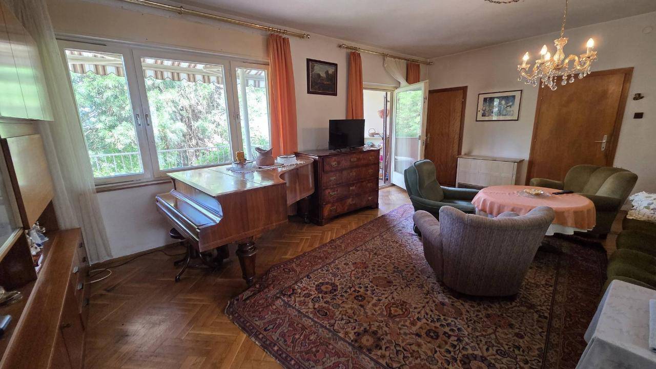 Gemütliches Wohnzimmer mit Fischgrätparkett, klassischer Einrichtung und Zugang zum Balkon.