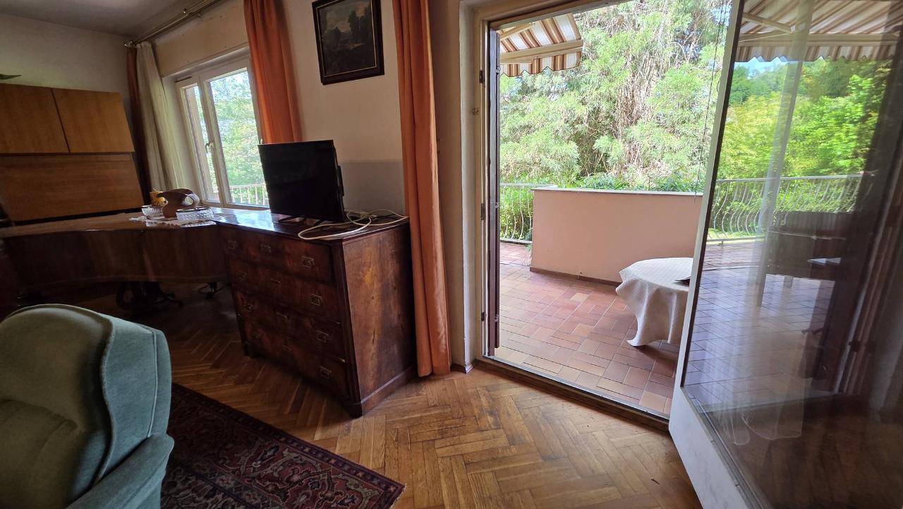 Blick vom Wohnzimmer auf den sonnigen Balkon mit üppigem Grün im Hintergrund.
