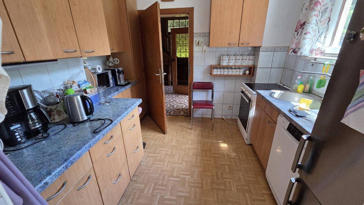 Funktionale Küche mit Holzschränken, Fliesenboden und Blick in den angrenzenden Essbereich.