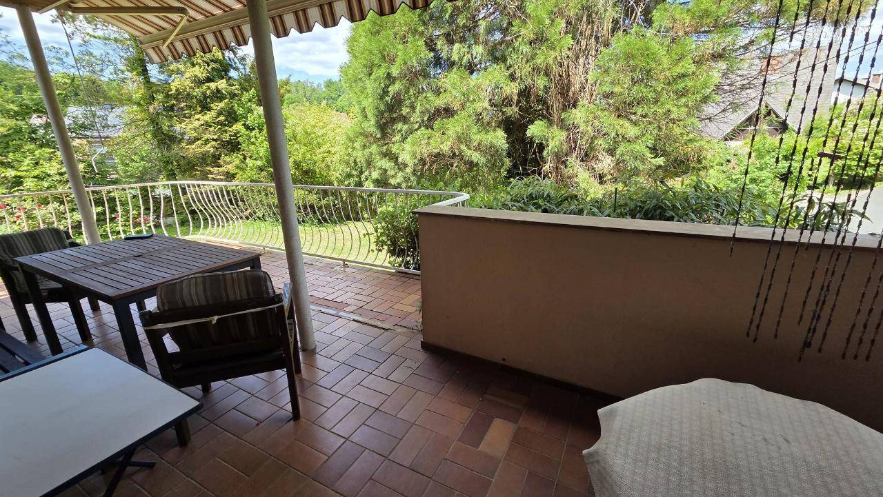 Überdachter Balkon mit Fliesenboden und Gartenmöbeln, ideal für Mahlzeiten im Freien.