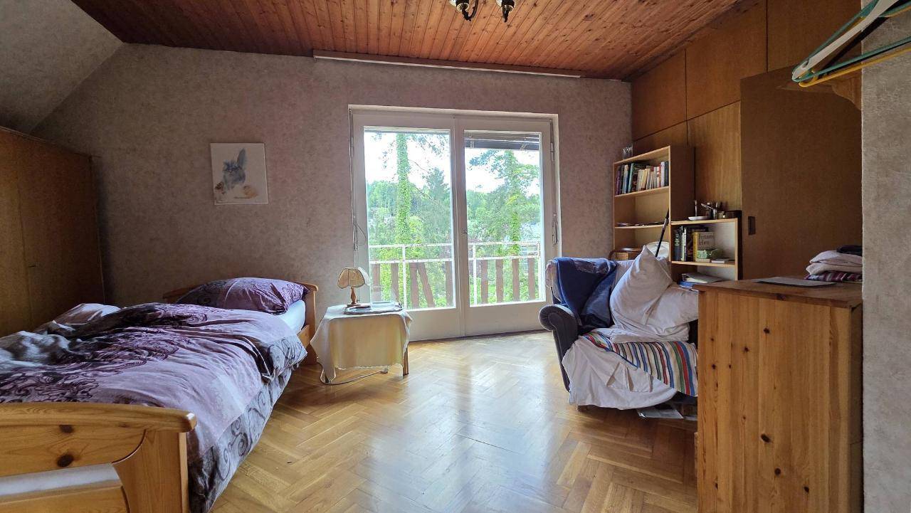 Schlafzimmer mit Holzboden, Holzdecke und großen Fenstern, die viel Tageslicht hereinlassen.