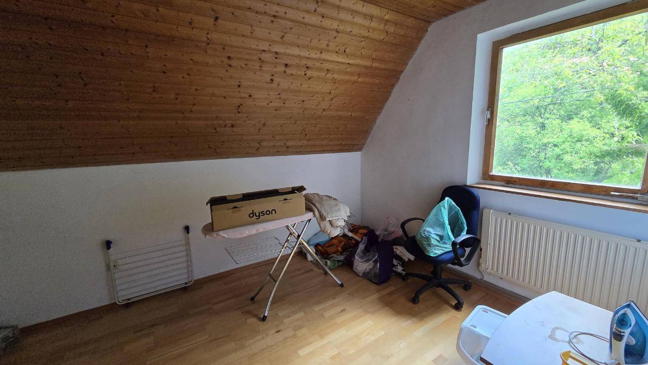 Dachzimmer mit Holzverkleidung an der Schräge und einem Fenster mit Blick ins Grüne.