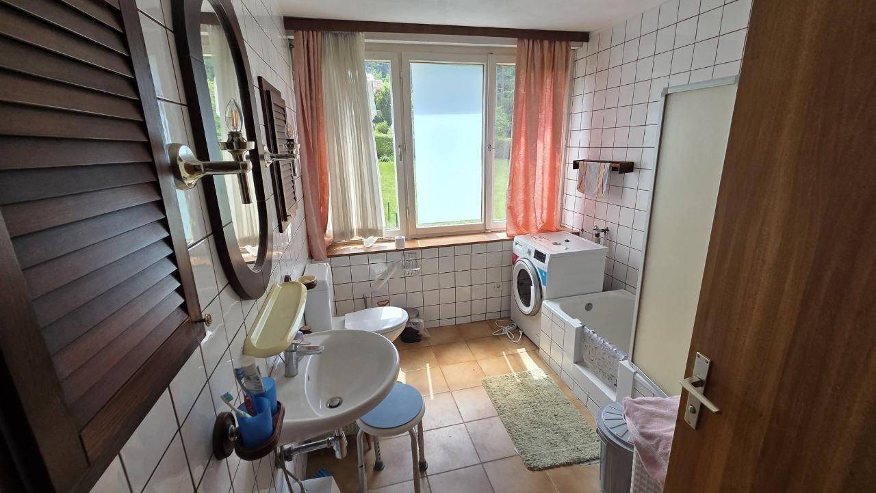 Helles Badezimmer mit weißen Fliesen, Waschbecken, Toilette und Badewanne mit Waschmaschine.
