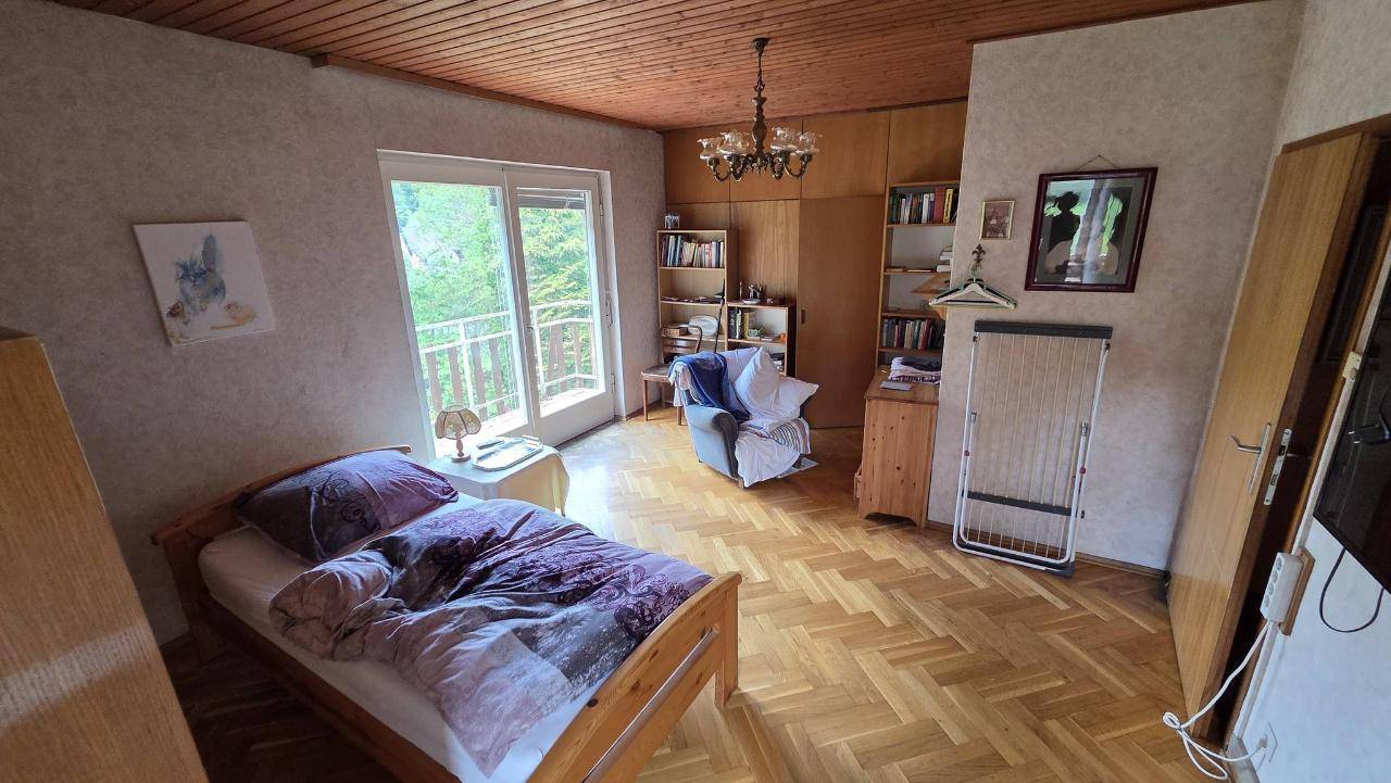 Gemütliches Schlafzimmer mit Parkettboden, Holzdecke und Zugang zu einem Balkon mit Waldblick.