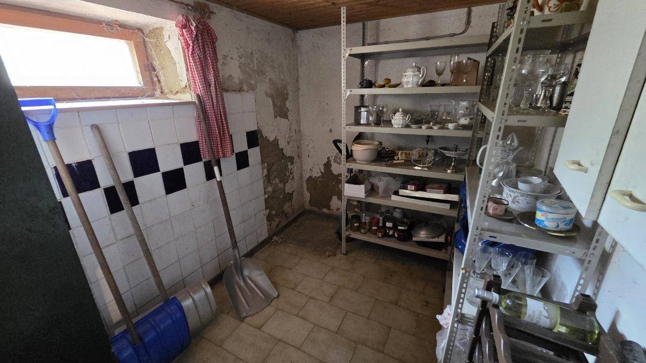 Kellerraum mit Regalen für Geschirr und Haushaltsgegenstände, gefliestem Boden und kleinem Fenster.
