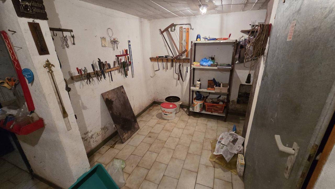 Werkstattraum im Keller mit Fliesenboden, Werkzeugen an der Wand und Regalen für Lagerung.