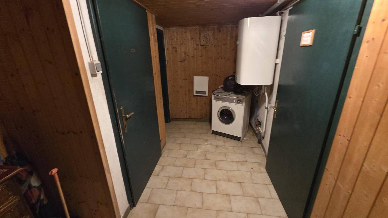 Hauswirtschaftsraum im Keller mit Waschmaschine, Warmwasserbereiter und Holzverkleidung an den Wänden.