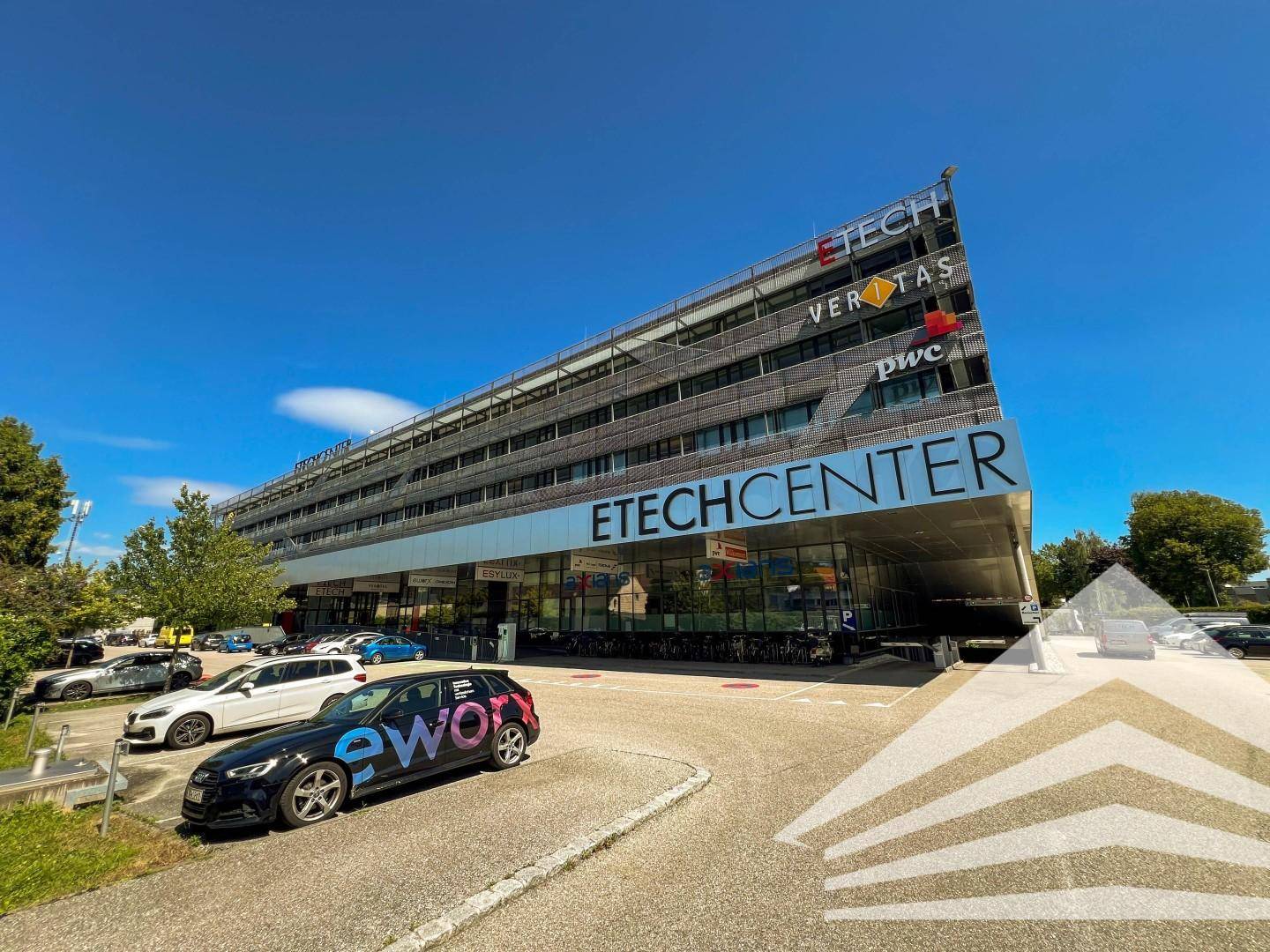 Modernes Geschäftsgebäude "ETECHCENTER" mit Glasfassade und Parkplätzen unter blauem Himmel.