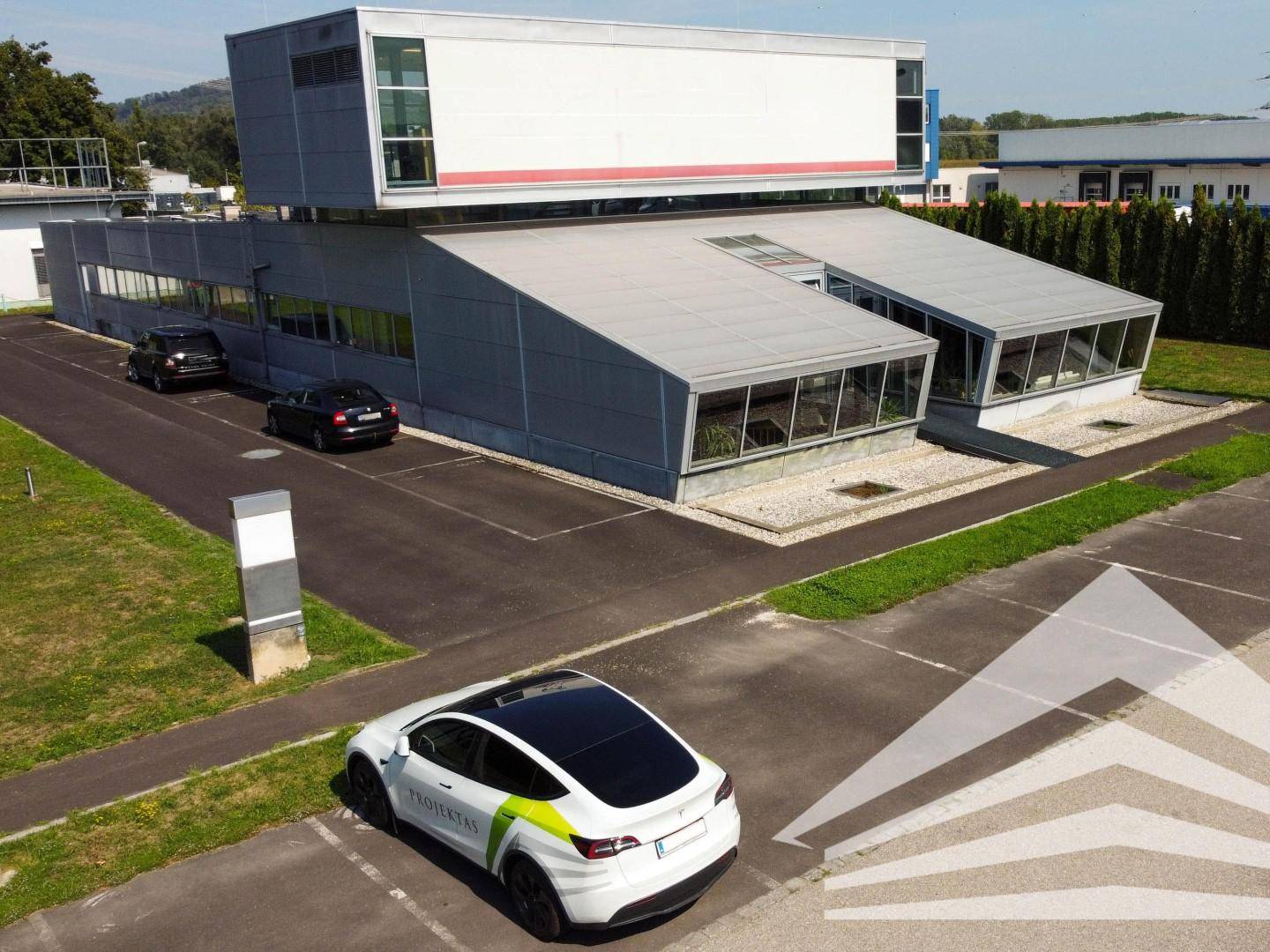 Gesamtansicht des modernen Bürogebäudes mit Parkplätzen, Grünflächen und Ladestation für Elektrofahrzeuge.