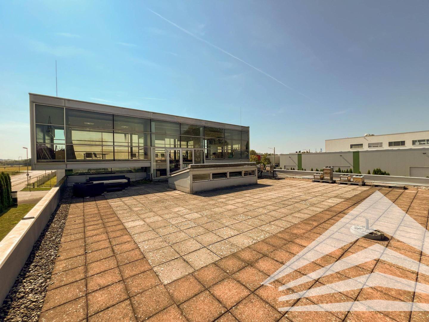 Weitläufige Dachterrasse mit Pflastersteinen und Blick auf die moderne Glasfassade des Gebäudes.