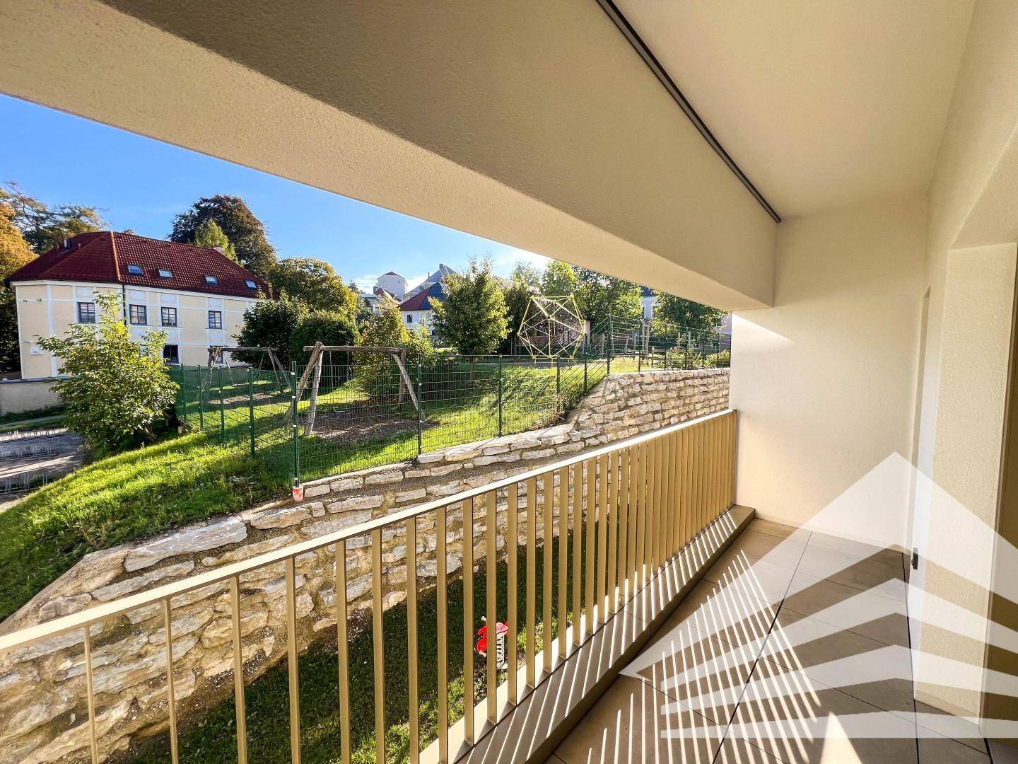 Geräumiger Balkon mit Blick auf einen Spielplatz und grüne Umgebung.