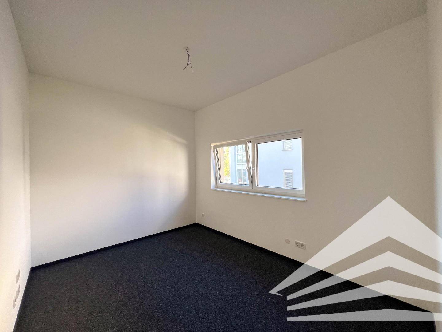 Helles Schlafzimmer mit Teppichboden und einem Fenster, das viel Tageslicht hereinlässt.