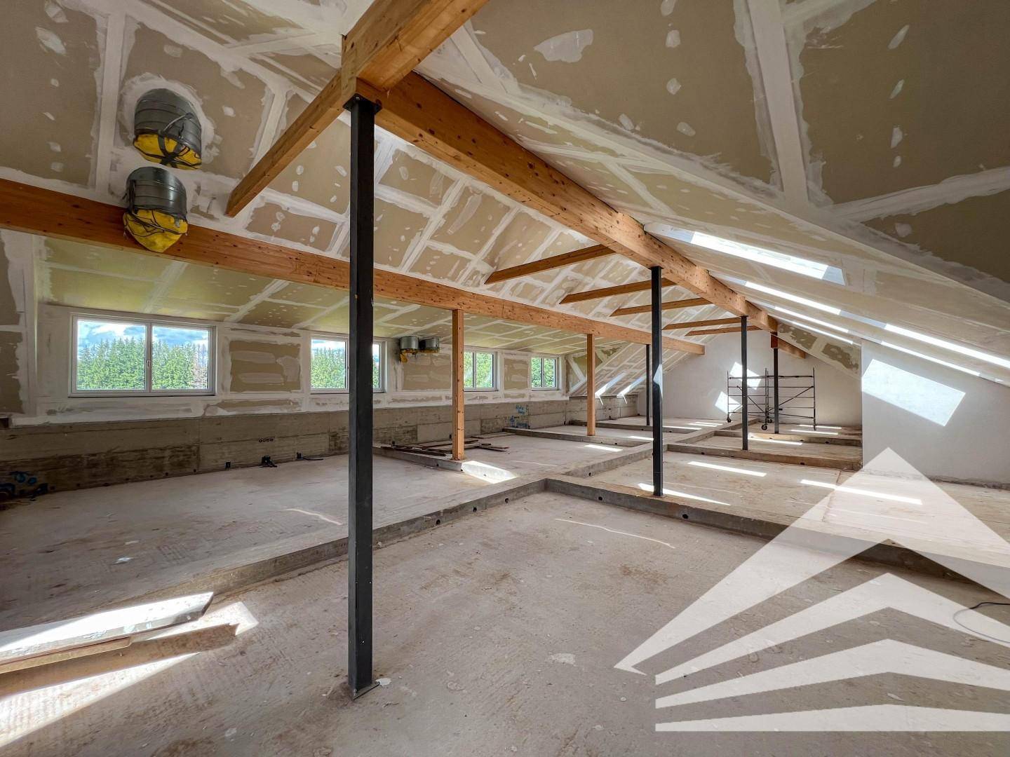 Dachgeschoss im Rohbau mit sichtbaren Holzbalken und Dachschrägen, bereit für den Ausbau.