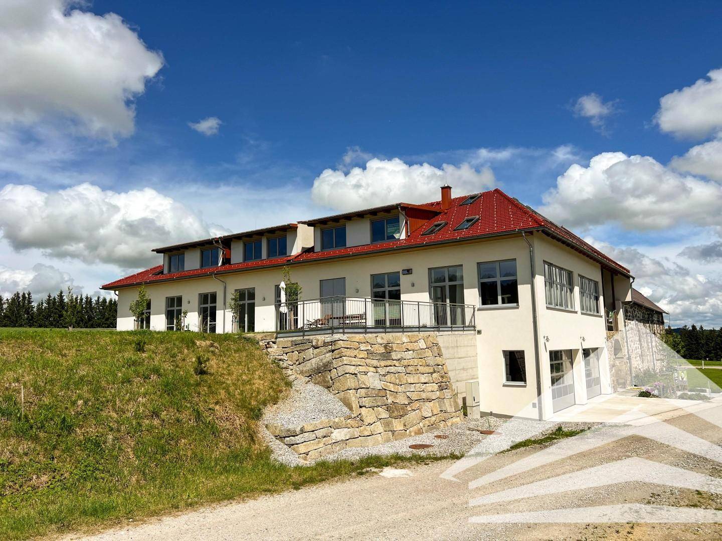 Modernes Gebäude mit rotem Ziegeldach und Terrassen, eingebettet in eine grüne Hügellandschaft.