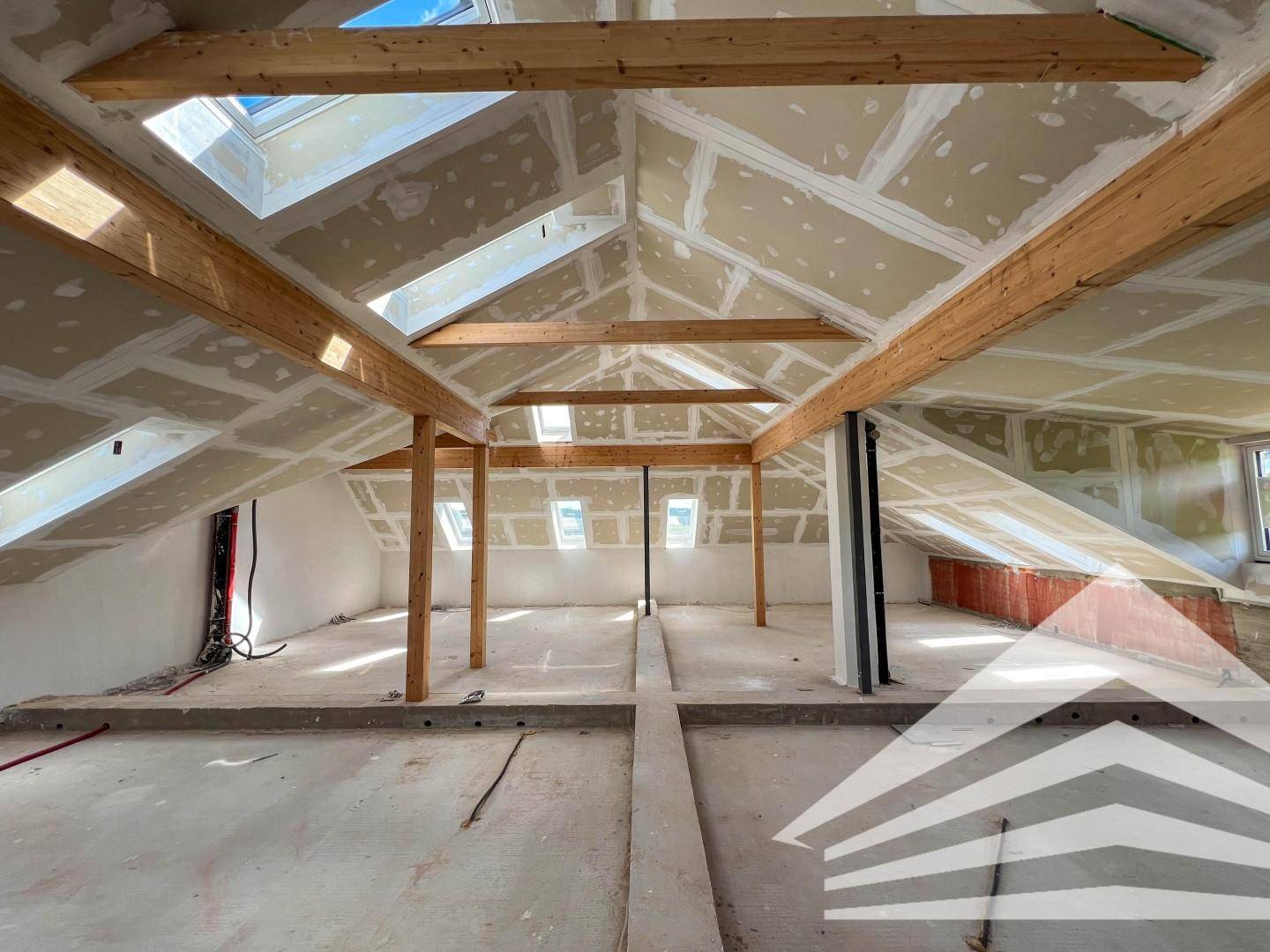 Unausgebauter Dachboden mit sichtbaren Holzbalken und Dachfenstern, bereit für den Ausbau.