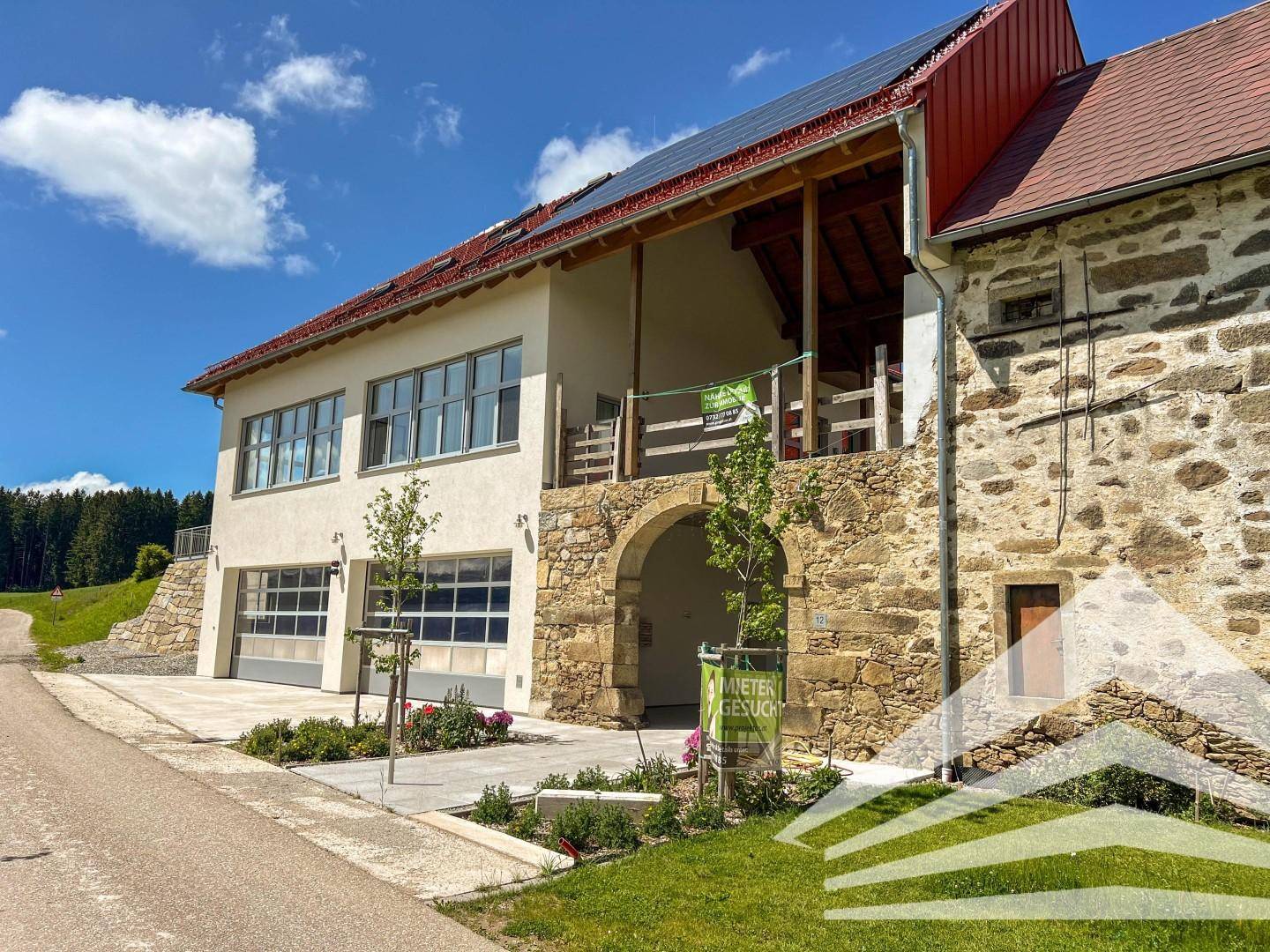 Historisches Gebäude mit moderner Erweiterung, Steinfassade, Garagen und Photovoltaikanlage auf dem Dach.