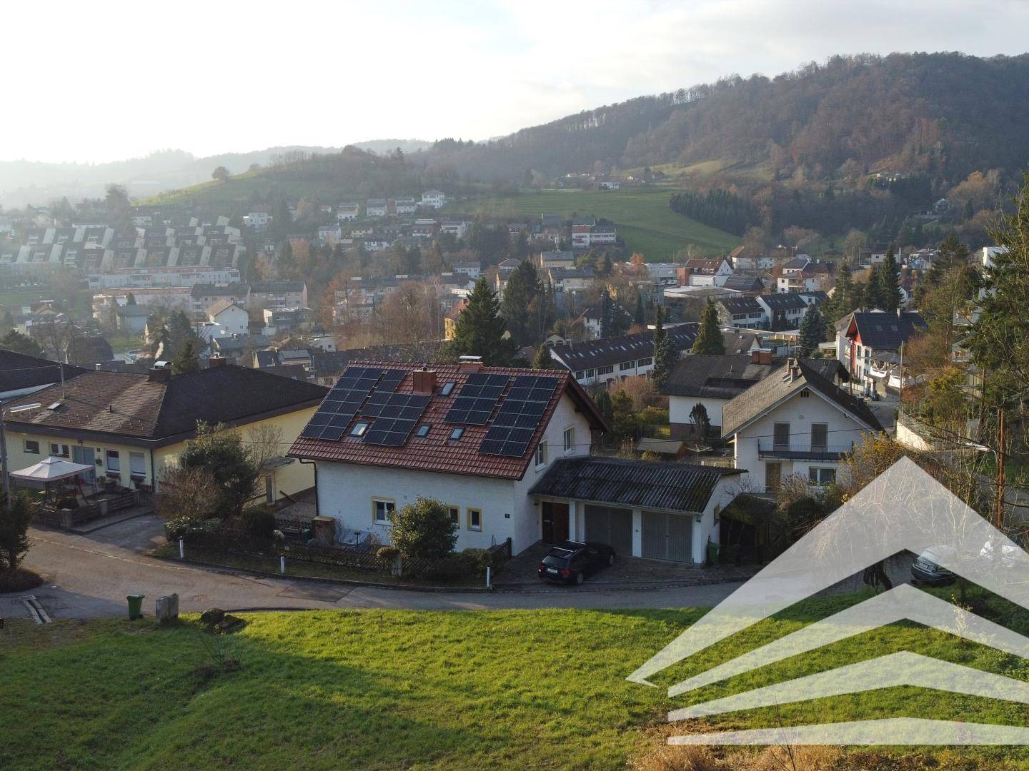 Panoramablick auf die Wohnsiedlung mit Einfamilienhäusern und grünen Hügeln im Hintergrund.