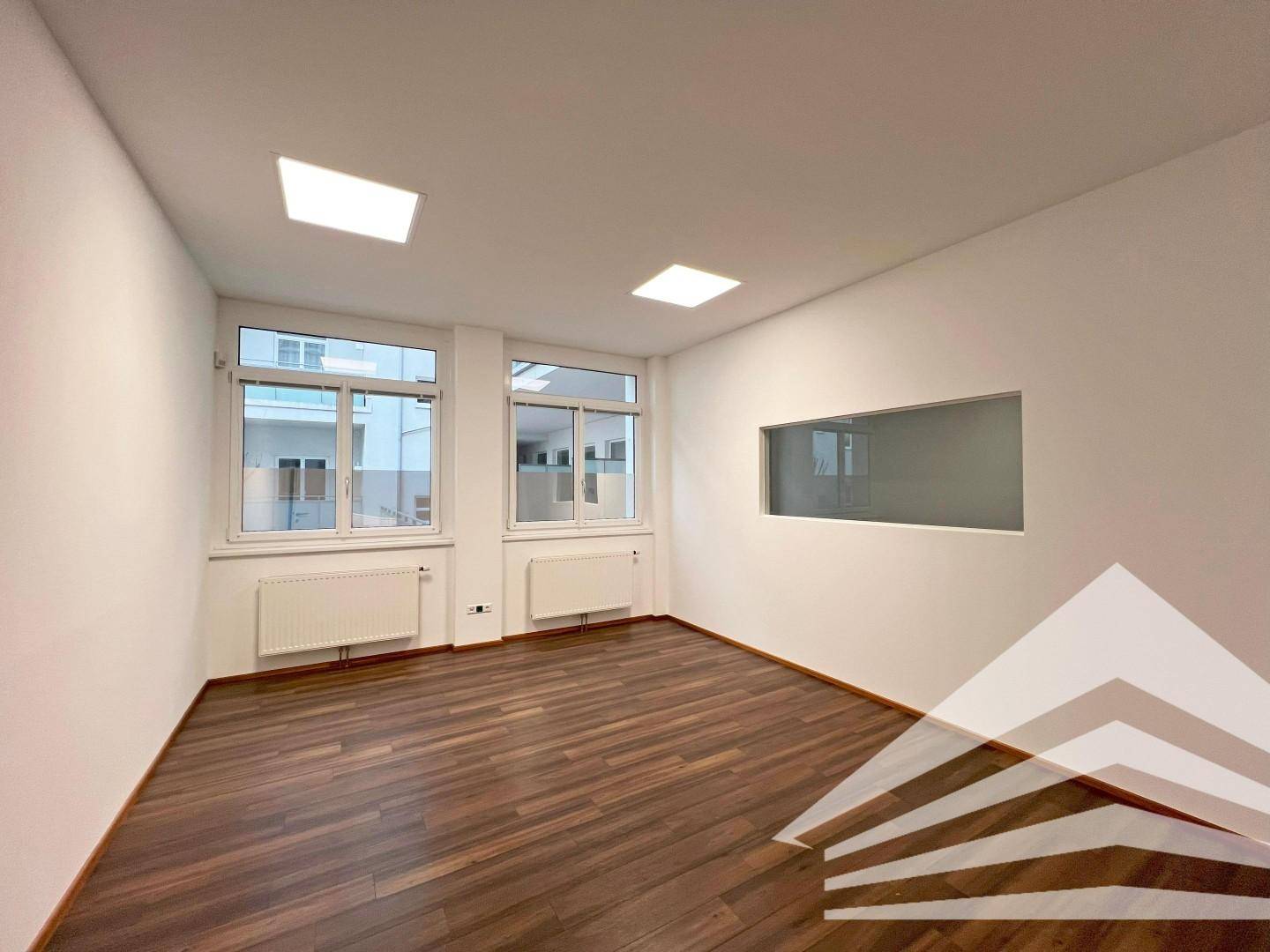 Büro mit zwei Fenstern und einer internen Glasöffnung, die für zusätzliche Helligkeit sorgt.