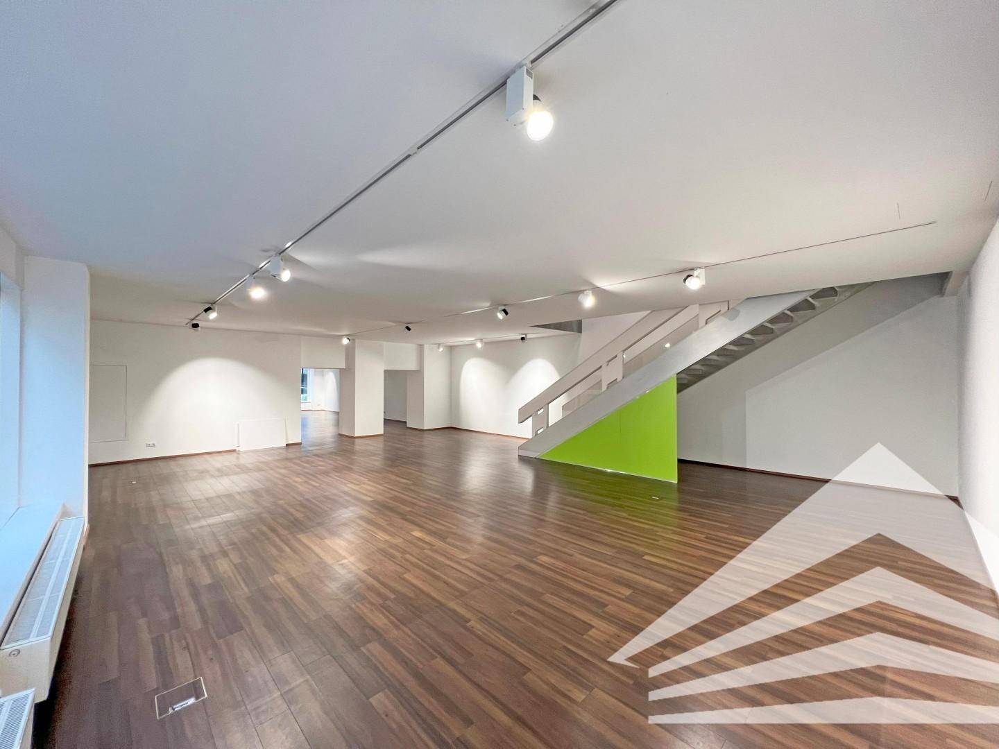 Moderner Geschäftsraum mit markanter grüner Akzentwand an der Treppe und Holzboden.