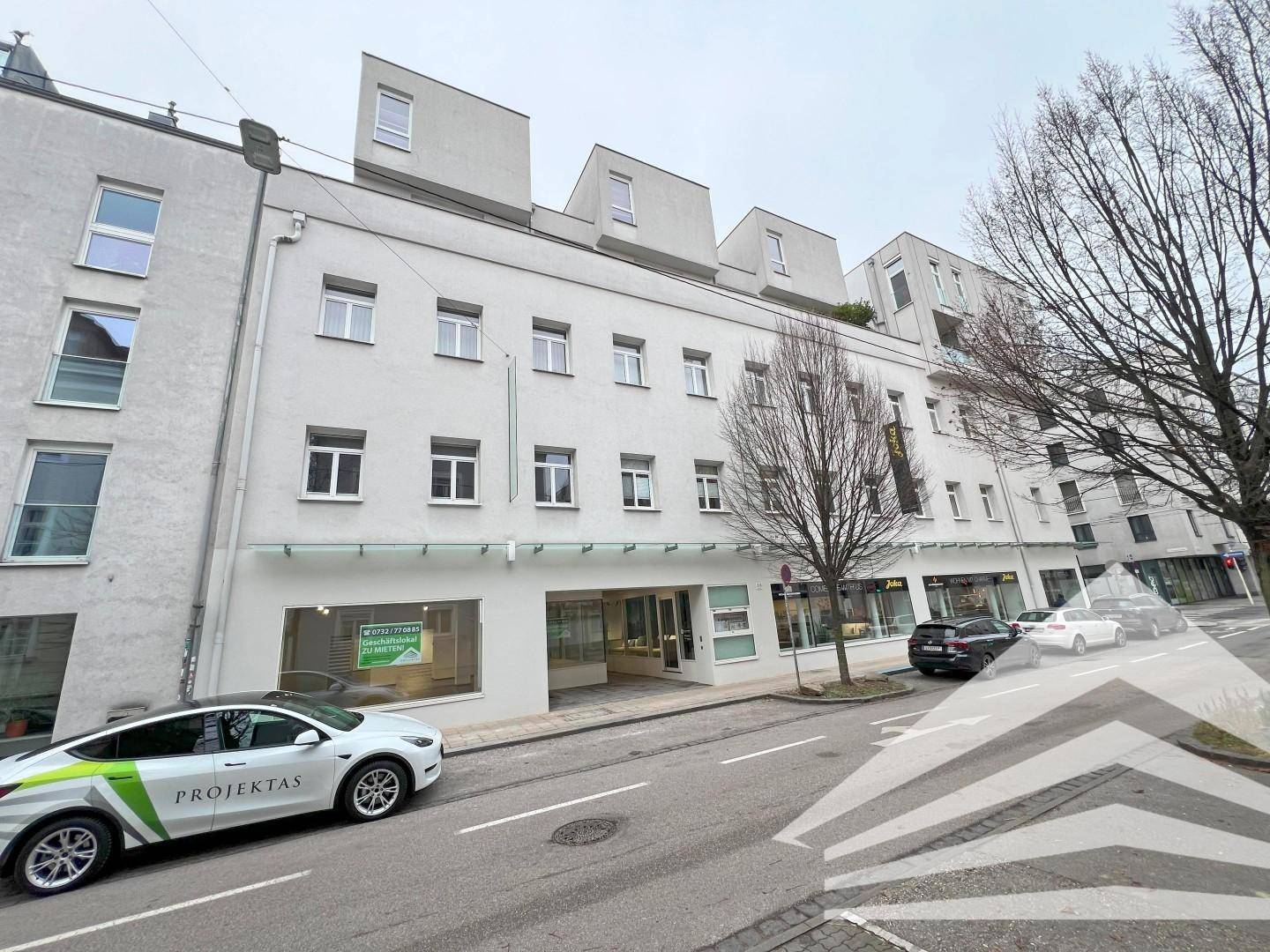Gesamtansicht des Geschäftsgebäudes von der Straße, mit modernen oberen Etagen und Geschäften im Erdgeschoss.
