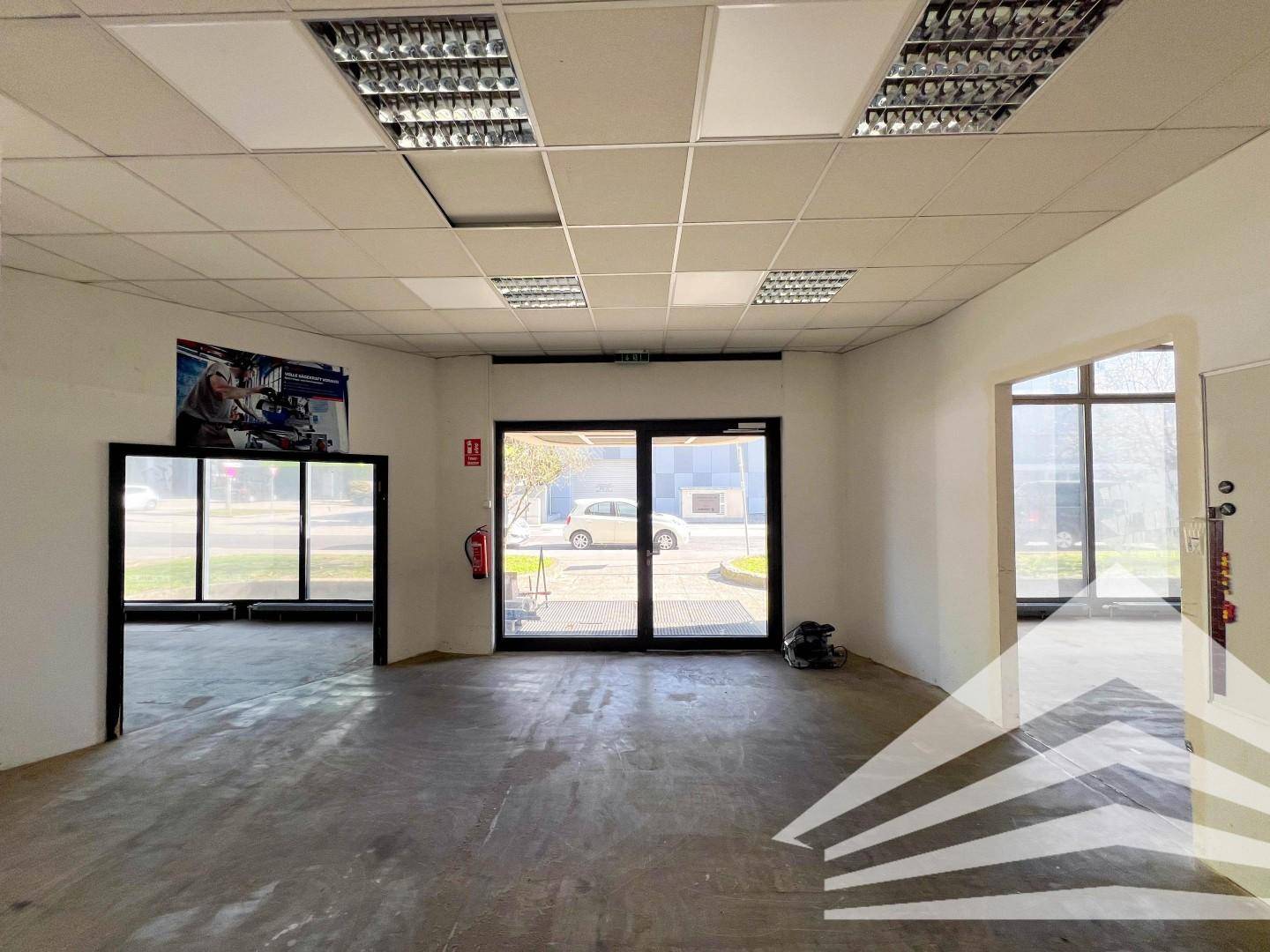 Eingangsbereich eines Gewerberaums mit großen Glastüren und Blick auf den Außenbereich, ausgestattet mit Rasterdecken.
