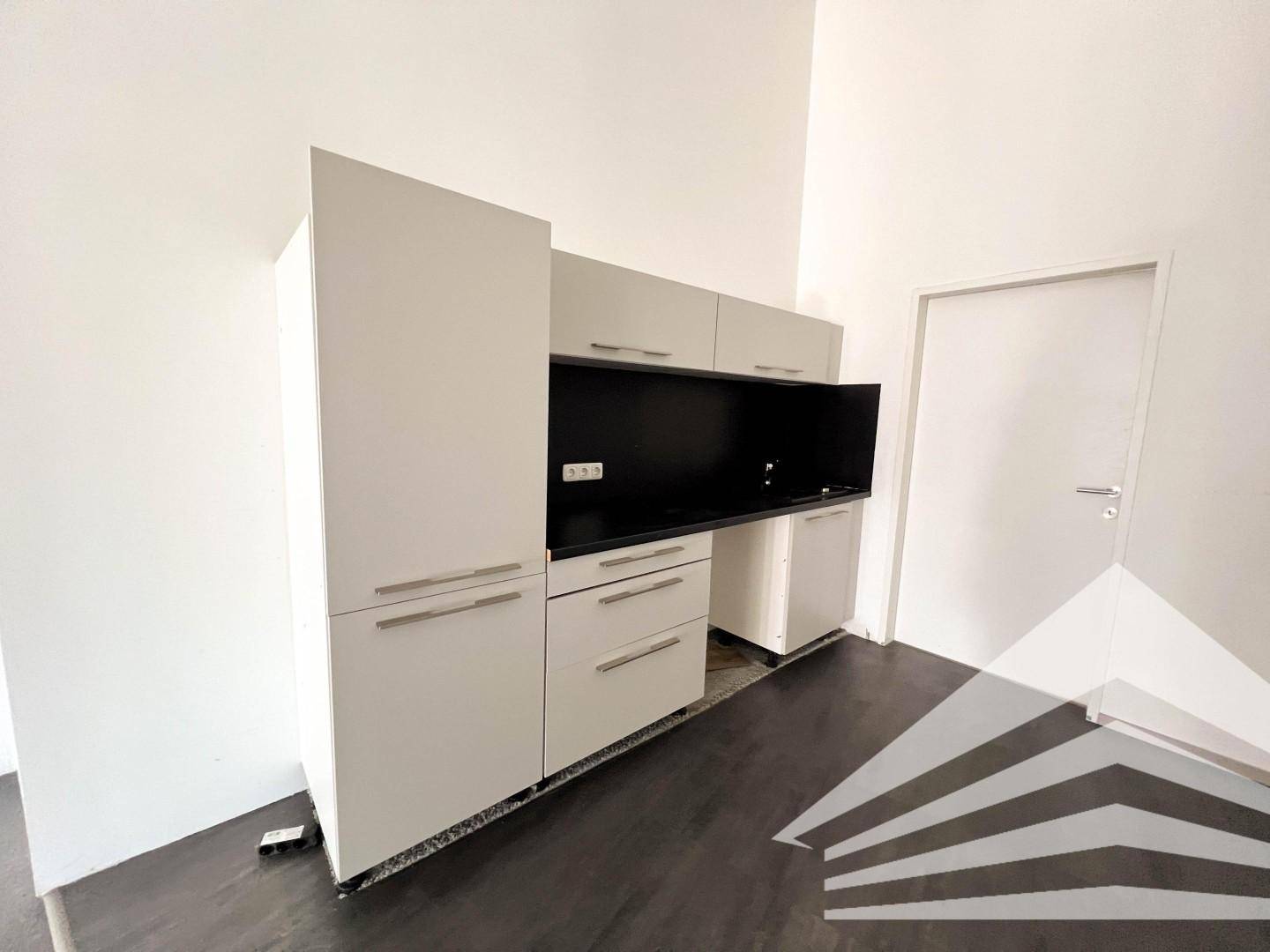 Funktionale Küchenzeile mit weißen Schränken und dunkler Arbeitsplatte, ideal für eine kleine Büroküche.