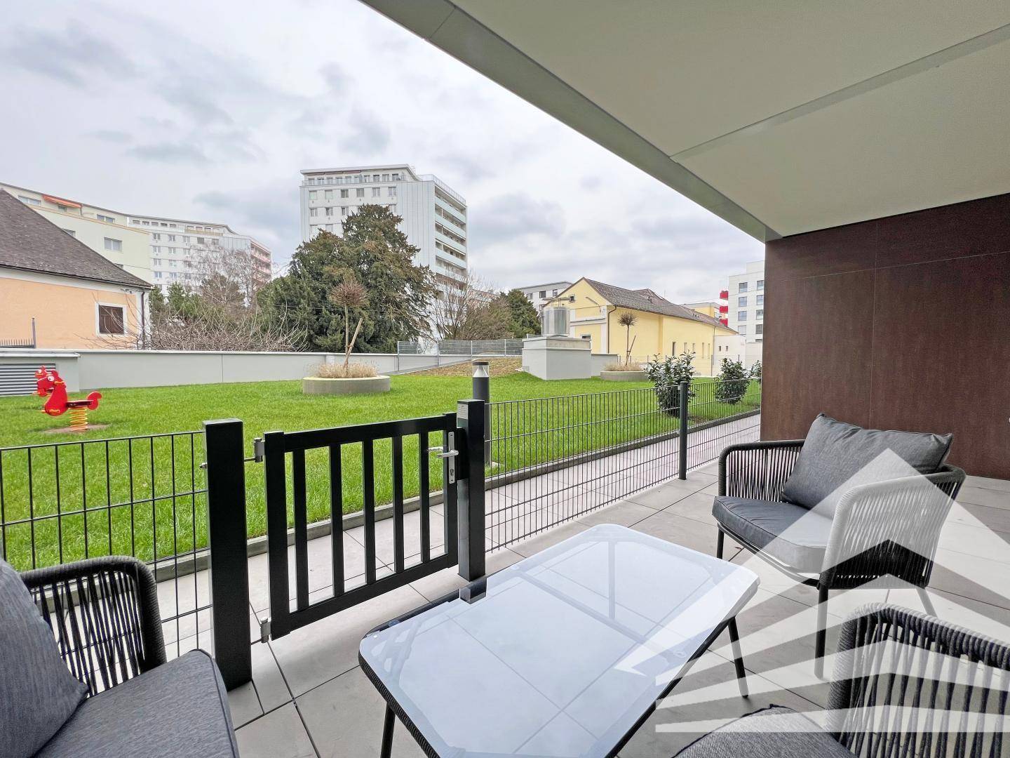 Sonniger Terrassenbereich mit Sitzgelegenheiten und Zugang zu einer kleinen Rasenfläche.