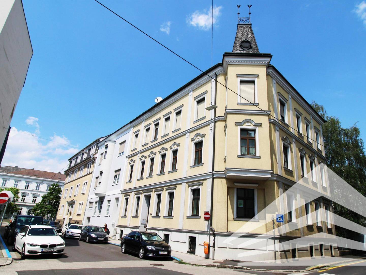 Historisches Eckgebäude mit gelber Fassade, vielen Fenstern und einem markanten Turm.