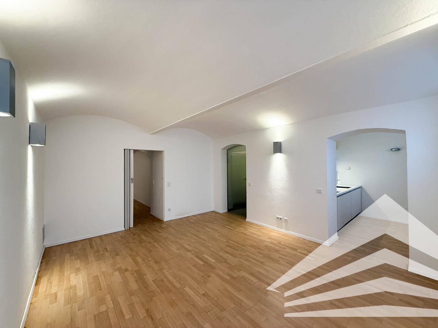 Heller Raum mit Holzboden und gewölbter Decke, bietet offene Übergänge zu weiteren Bereichen.