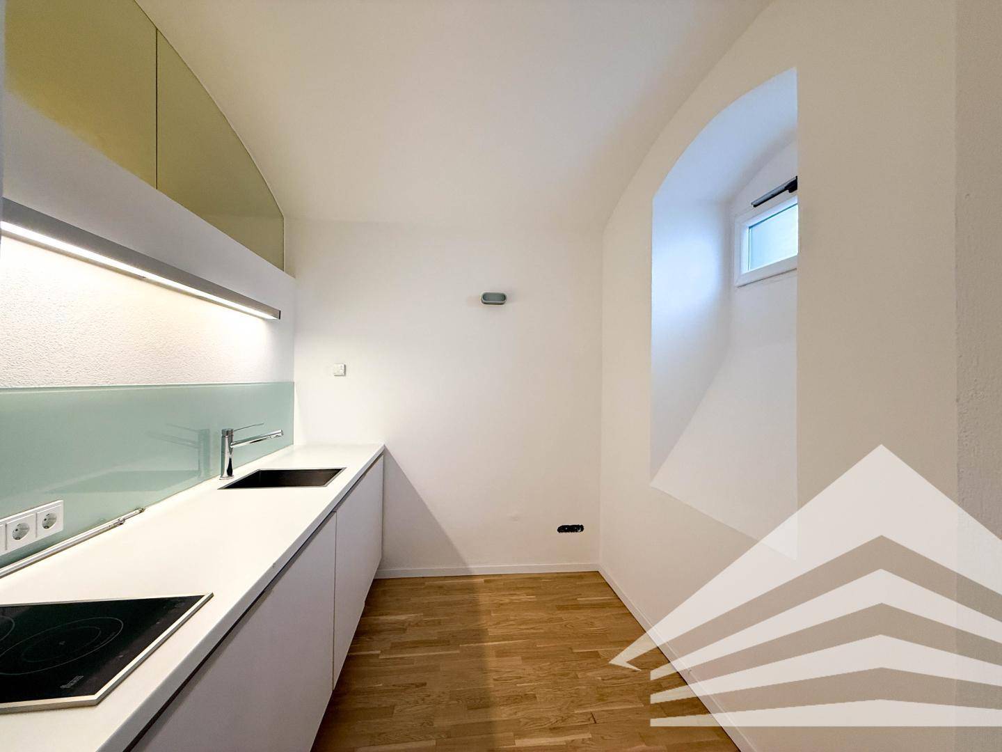 Moderne Küchenzeile mit weißen Schränken, Induktionskochfeld und kleinem Bogenfenster.