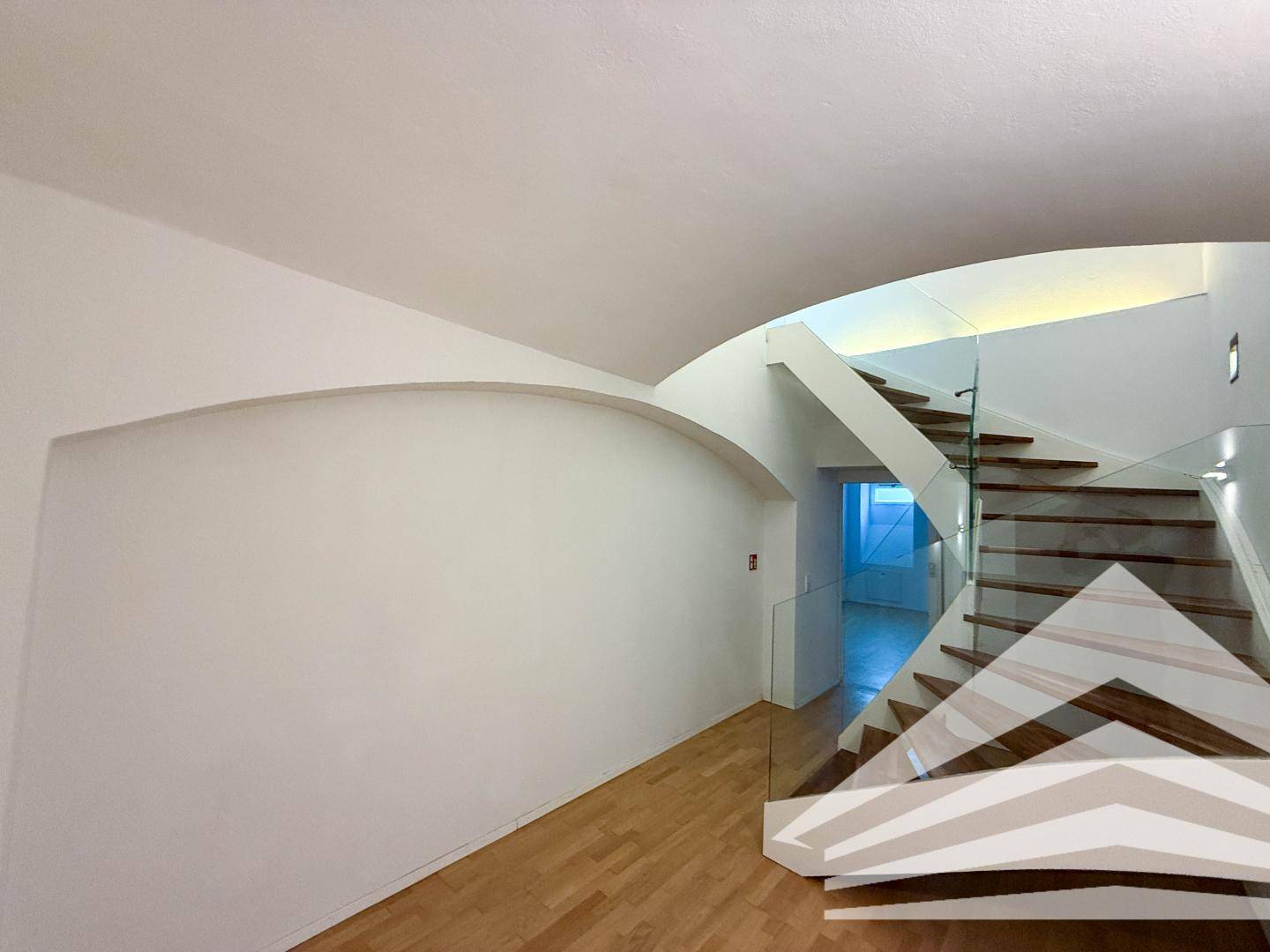 Stilvolle Holztreppe mit Glasgeländer in einem hellen Flur mit gewölbter Decke.