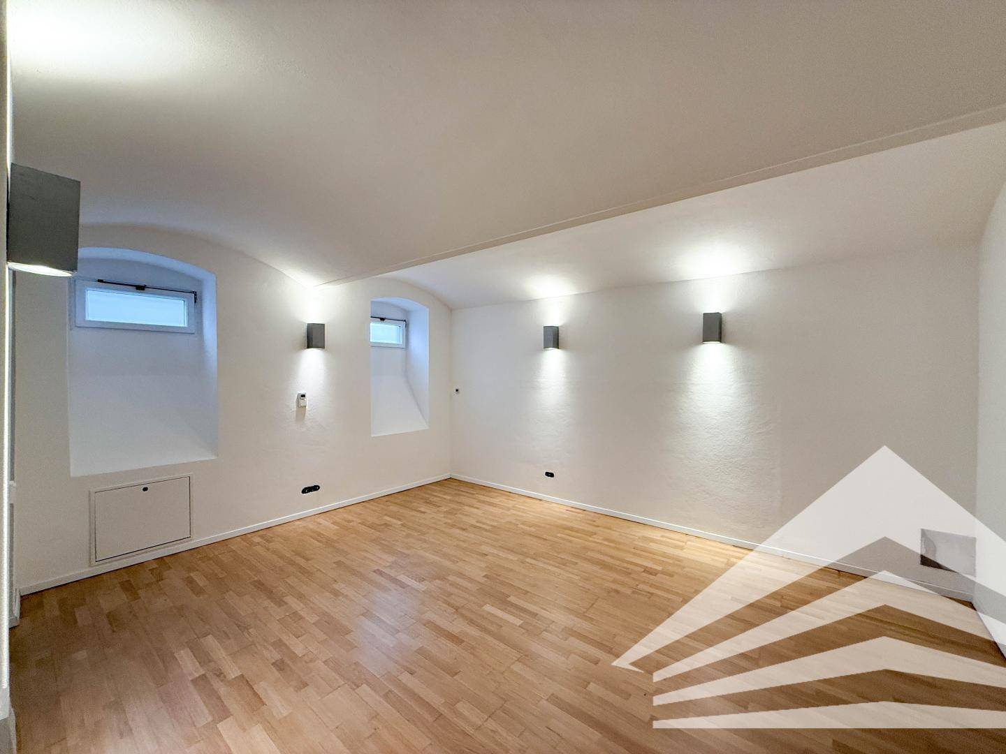 Heller Raum im Untergeschoss mit Holzboden und zwei kleinen Bogenfenstern, vielseitig nutzbar.