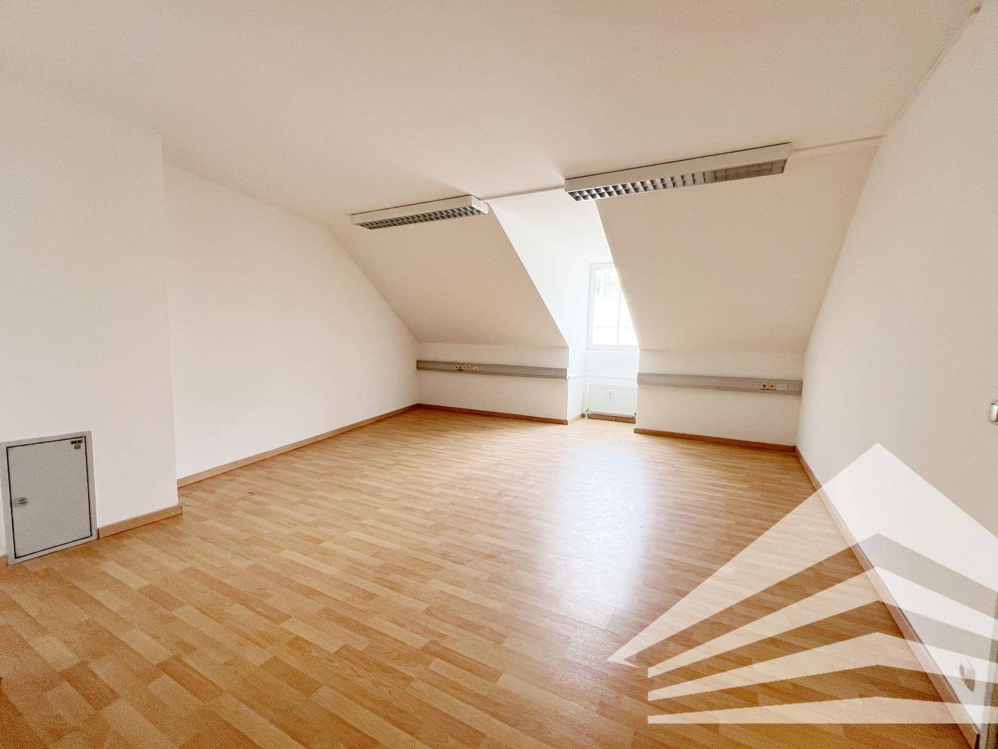 Heller, leerer Raum mit Dachschrägen, Laminatboden und weißen Wänden, geeignet als Arbeitsbereich.