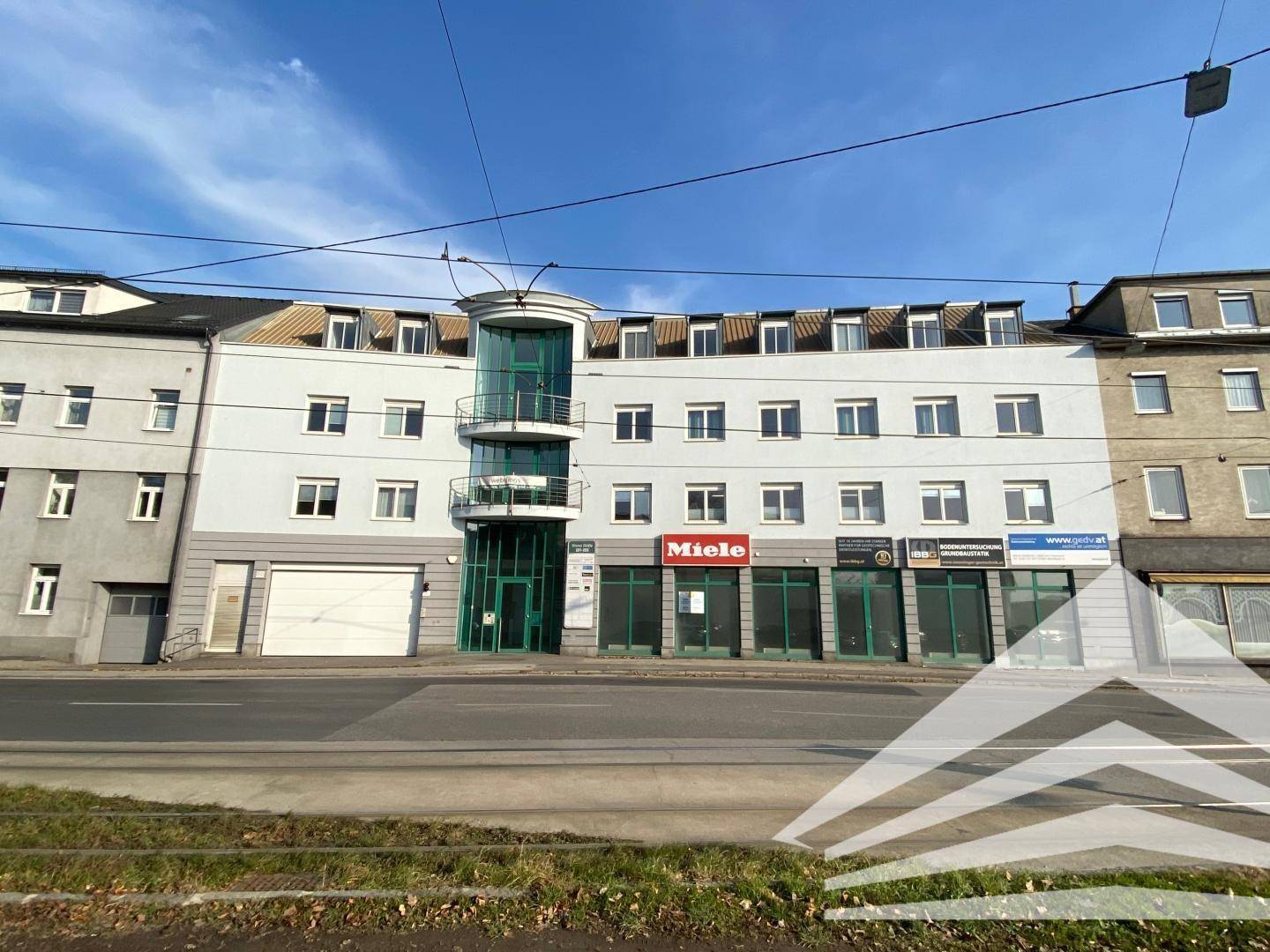 Mehrstöckiges Gebäude mit heller Fassade, vielen Fenstern und einer markanten grünen Glasrotunde an der Vorderseite.