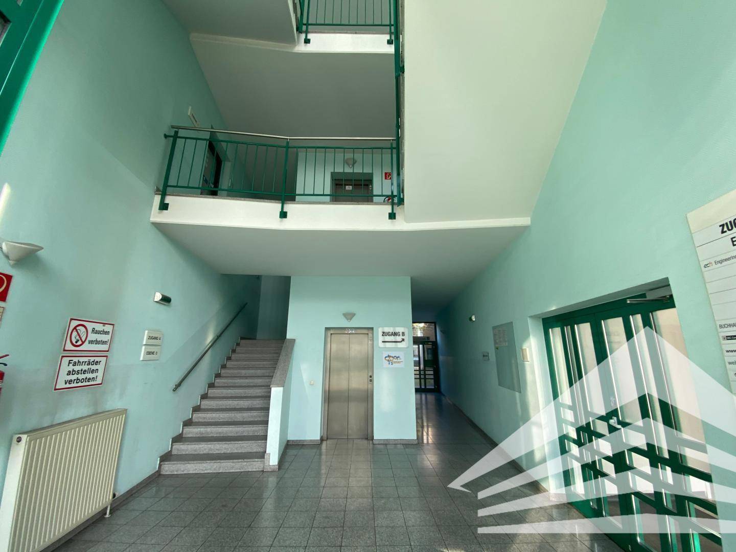 Eingangsbereich mit Treppe, Aufzug und Flur, gestaltet in hellgrünen Wänden und Fliesenboden.