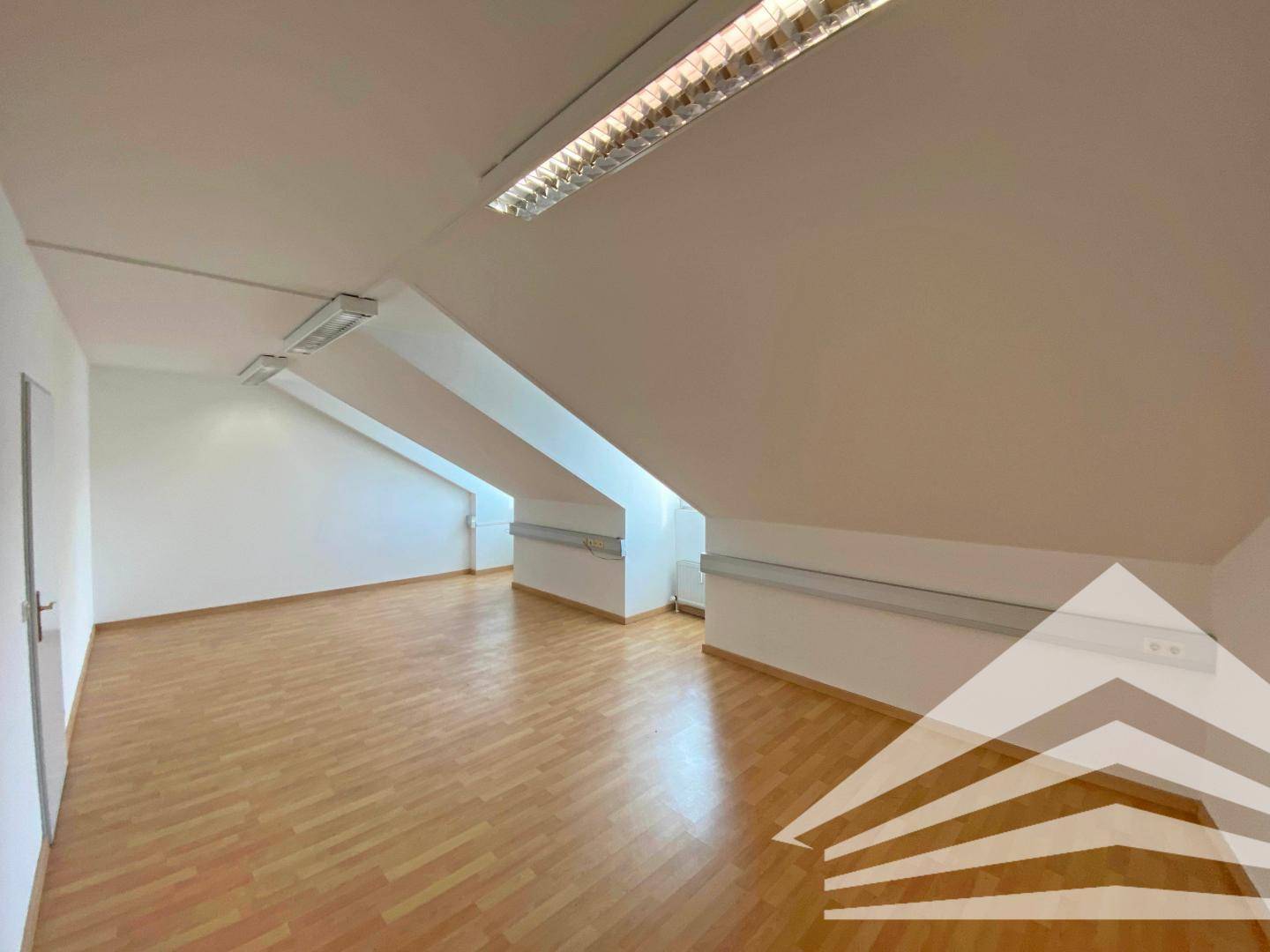 Weitläufiger, leerer Raum mit markanten Dachschrägen und hellem Laminatboden, ideal für flexible Nutzung.