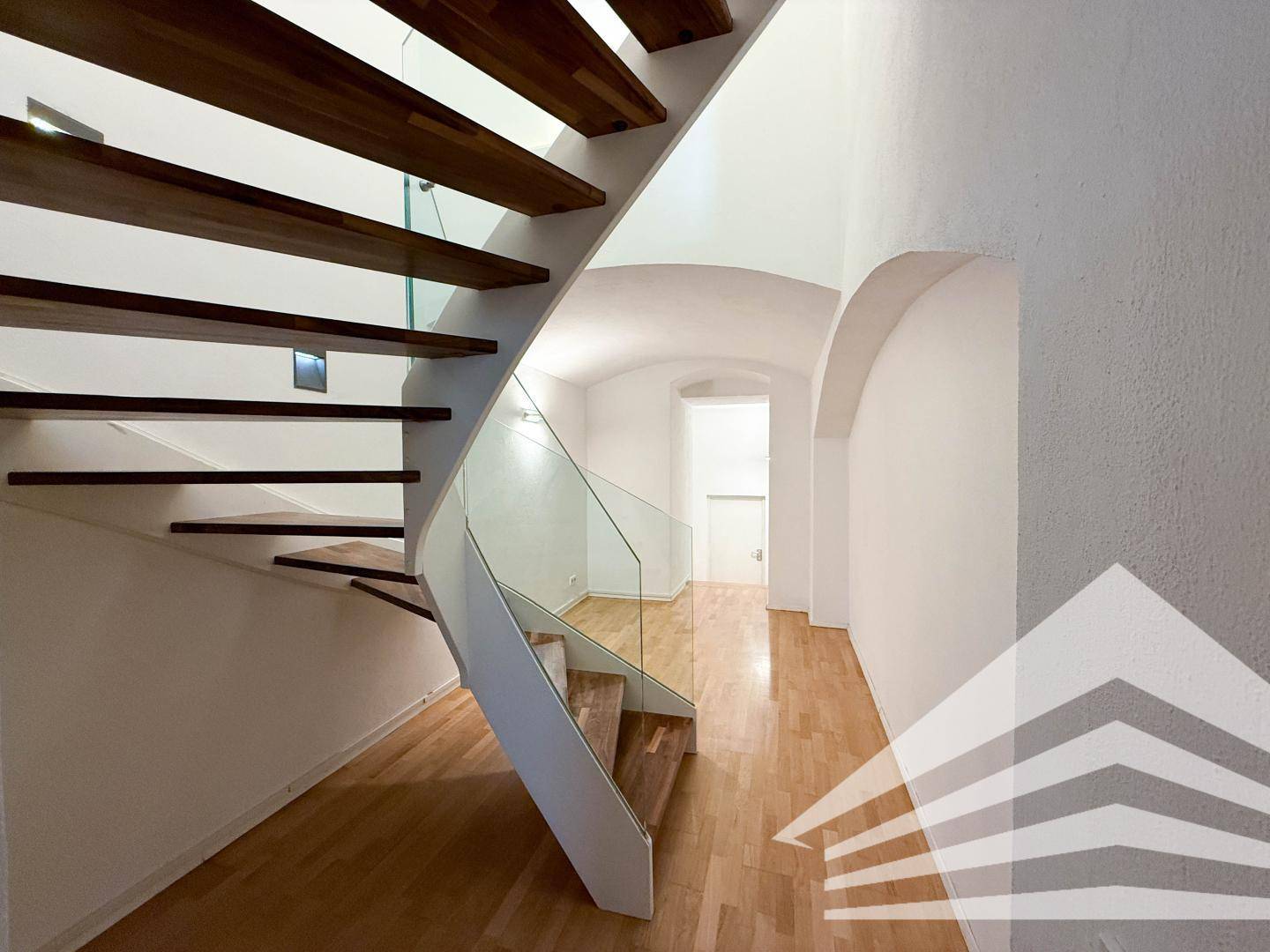 Elegante Holztreppe mit Glasgeländer, die zu den oberen Etagen führt, in einem hellen Flur.