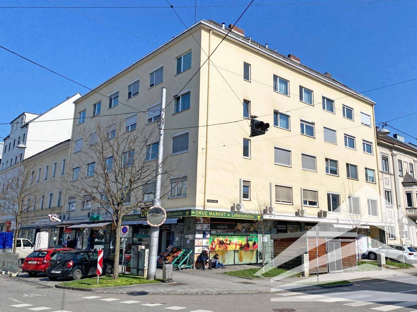 Mehrstöckiges Gebäude an einer Straßenecke mit Geschäften im Erdgeschoss und Wohnungen darüber.