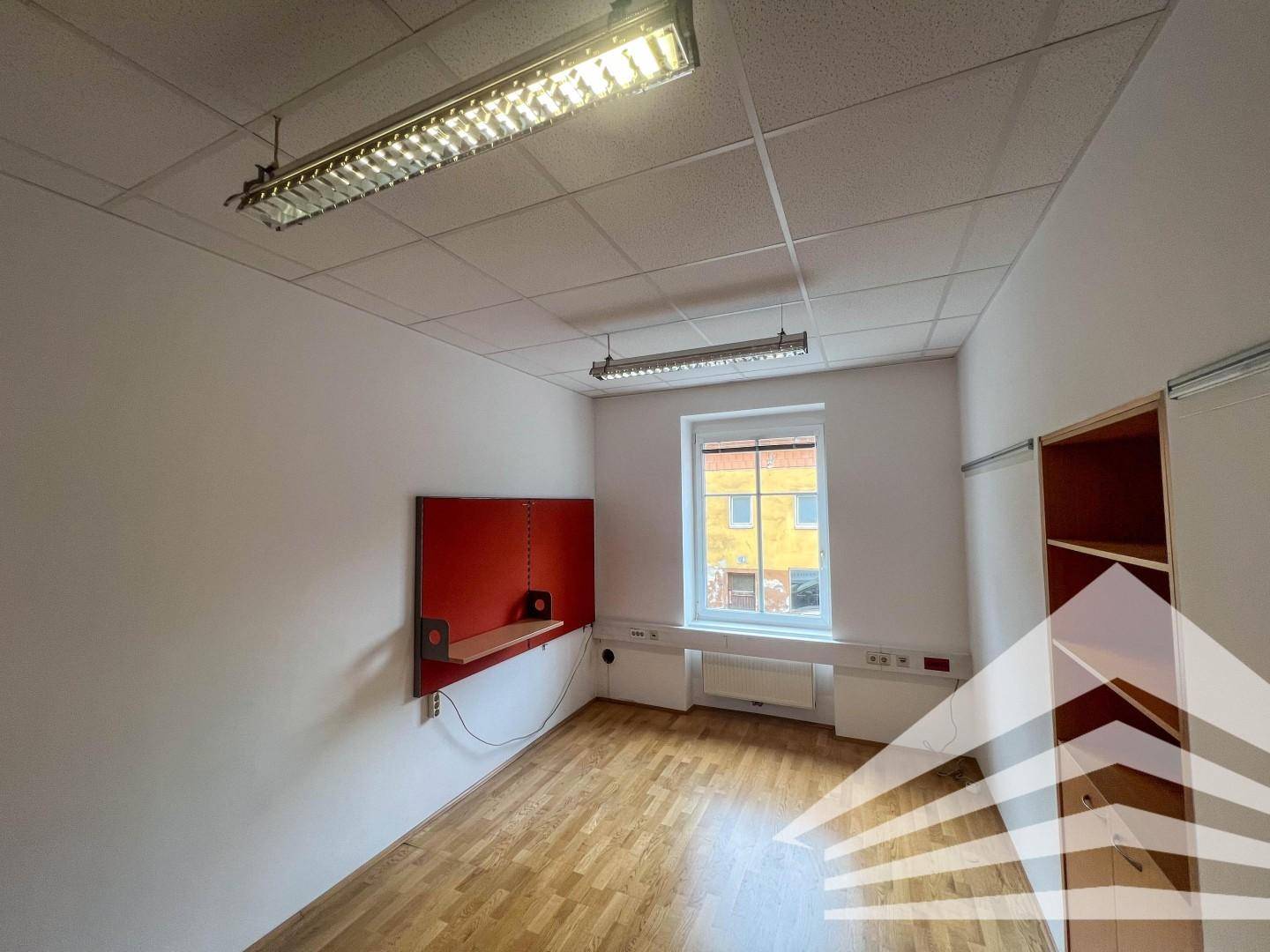 Büroraum mit einer roten Wandtafel, einem Fenster und einem hellen Holzfußboden.