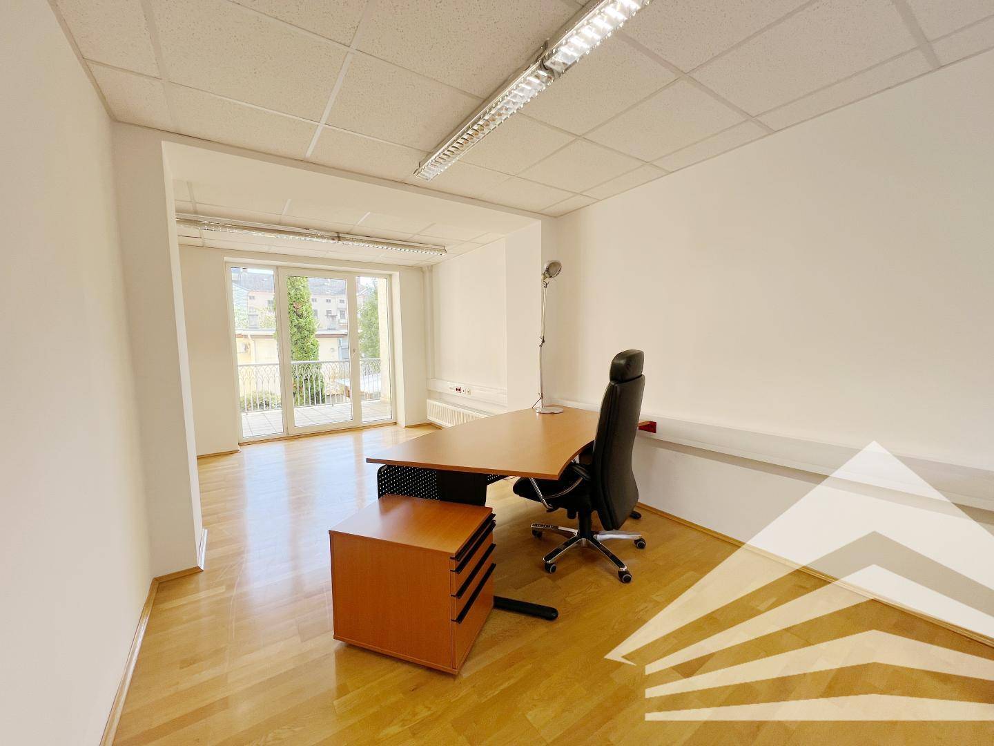 Helles Büro mit Schreibtisch, Bürostuhl und Zugang zu einem Balkon, ausgestattet mit Holzfußboden.