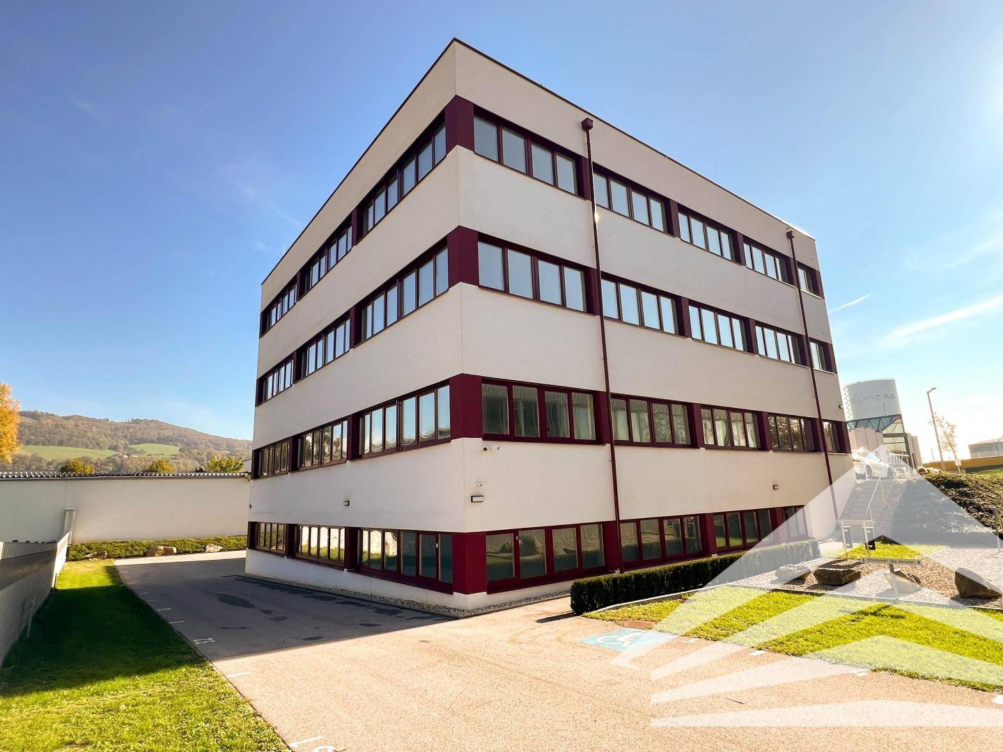 Modernes Bürogebäude mit vielen Fenstern und roter Akzentuierung, umgeben von gepflegten Grünflächen.