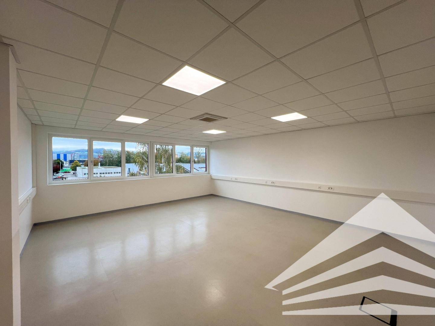 Leerer Büroraum mit einer langen Fensterfront, die den Blick auf die umliegende Landschaft freigibt.