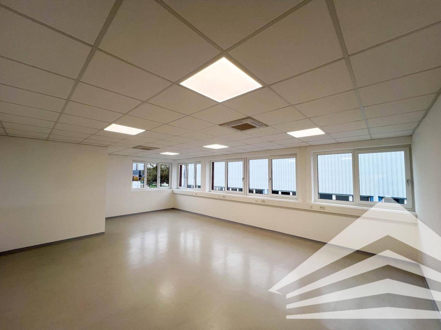 Großer Büroraum mit zahlreichen Fenstern und Blick auf angrenzende Gebäude.