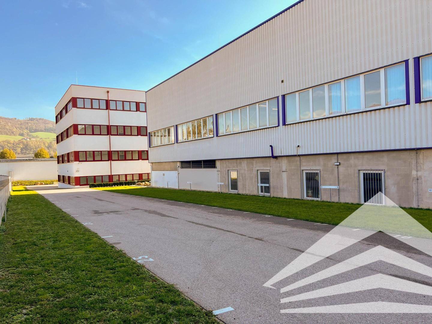 Außenansicht des modernen Bürogebäudes mit angrenzendem Parkplatz und gepflegten Grünflächen.