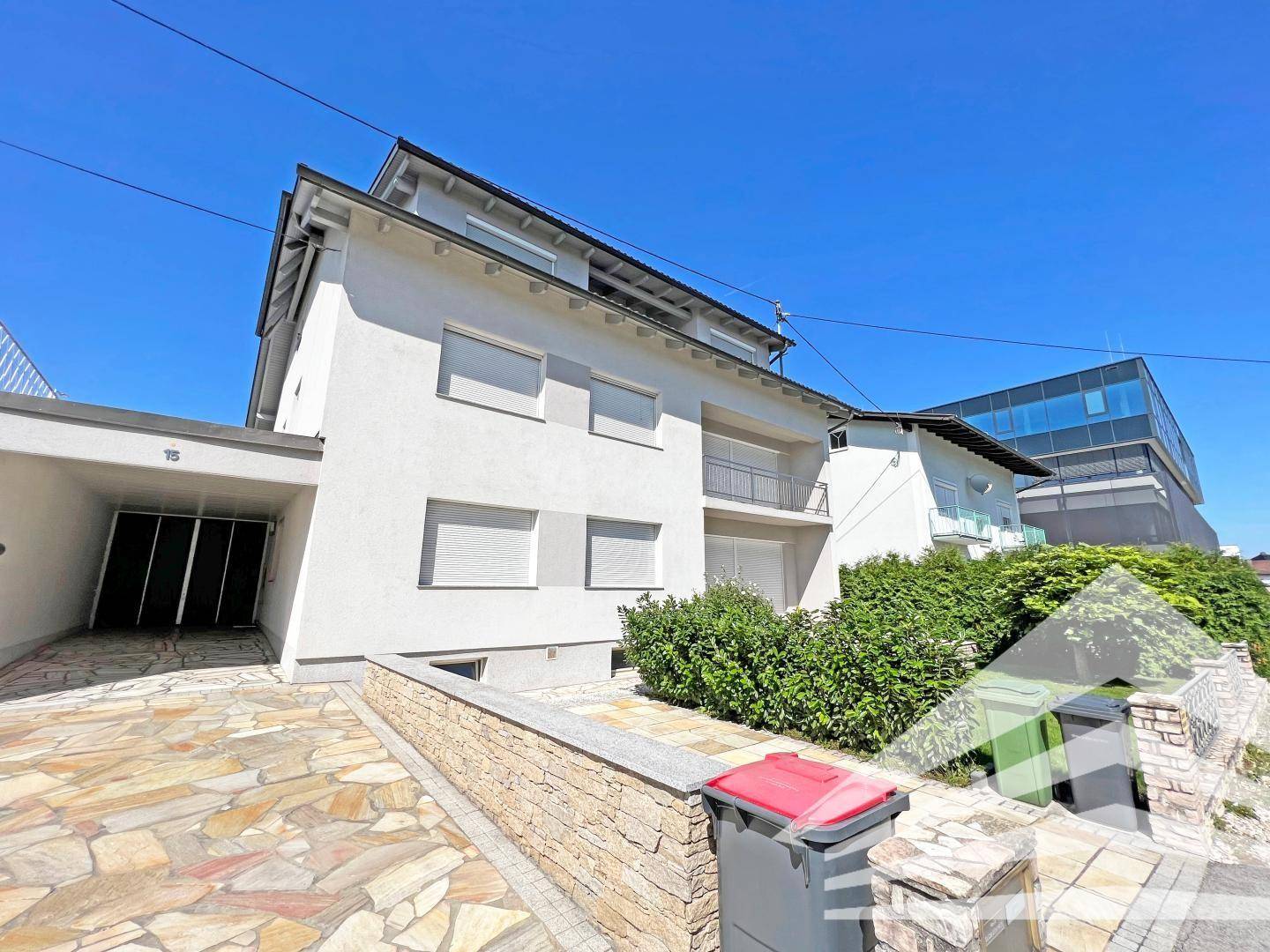 Moderne Hausfassade mit Carport und gepflasterter Auffahrt.