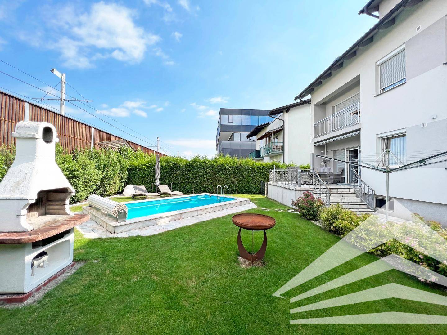 Gepflegter Garten mit Pool, Grillplatz und Liegestühlen unter blauem Himmel.