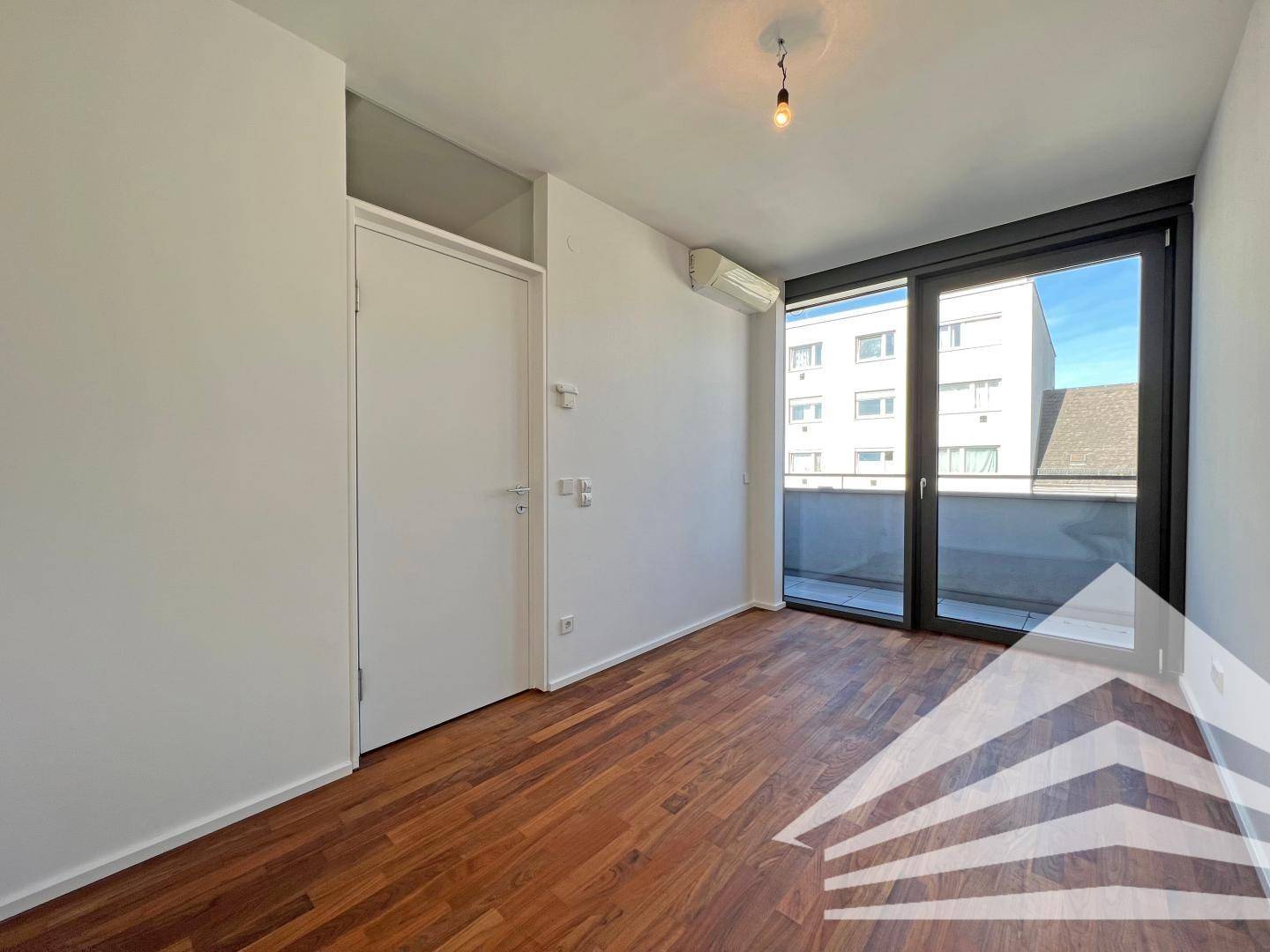 Heller Raum mit Holzboden und Zugang zu einem Balkon, ideal als Büro oder Schlafzimmer.