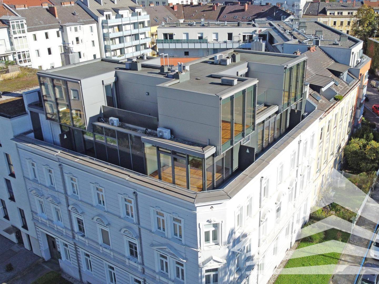 Dachaufbauten mit großen Glasflächen auf einem historischen Gebäude, umgeben von städtischer Architektur.
